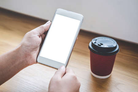 Image of Young woman looking at screen with a clean white screen and blank space for text, hand holding smartphone and typing with information and coffee cup in modern workspace.の写真素材