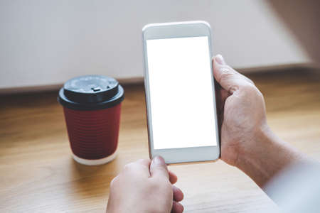 Image of Young woman looking at screen with a clean white screen and blank space for text, hand holding smartphone and typing with information and coffee cup in modern workspace.の写真素材