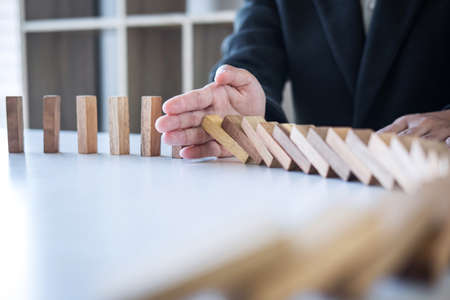 Risk and Strategy in Business, Image of hand stopping falling collapse wooden block dominoes effect from continuous toppled block, prevention and development to stability.の写真素材