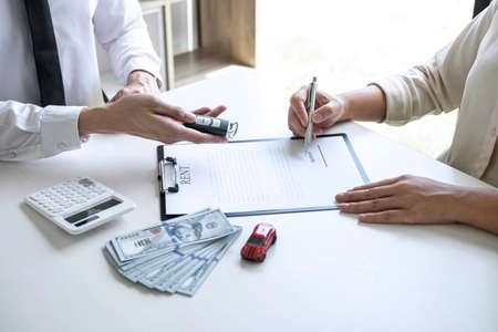 Car rent agent manager holding key of new car giving to woman client after signing good deal agreement contract, renting considering vehicle.の写真素材