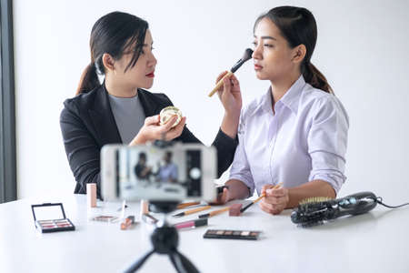 Business online on social media, Two Beautiful Woman Blogger is showing present tutorial beauty cosmetic product and broadcast live streaming video to social network while recording teaching online.の写真素材
