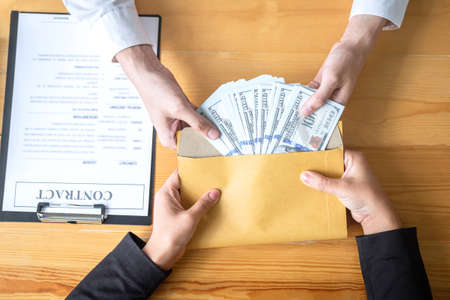Dishonest cheating in business illegal money, Businessman giving bribe money in envelope to business people to give success the deal contract of investment, Bribery and corruption concept.の写真素材