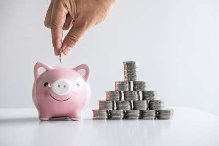 Images of stacking coins pile and Hand putting coin into pink piggy bank for planning step up to growing and savings with money box, Saving money for future plan and retirement fund concept.の写真素材
