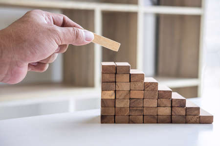 Alternative Risk and Strategy in business to make growth, Image of Business man's hand placing making a wooden block stacking hierarchy on growing to lay the foundation and development to successful.の写真素材