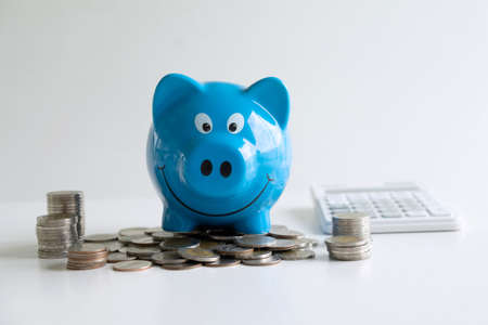 Images of stacking coins pile and blue smiling piggy bank to growing and savings with money box, Saving money for future plan and retirement fund concept.の写真素材