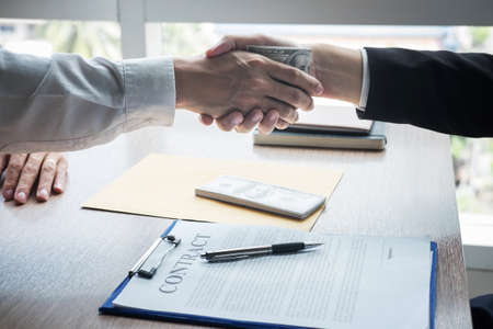 Dishonest cheating in business illegal money, Businessman handshake with money of dollar banknotes in hands from while give success the deal, Bribery and corruption concept.の写真素材