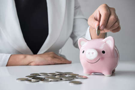 Business woman putting coin into pink piggy bank for planning step up growing business to profit and saving with piggy bank, Saving money for future plan and retirement fund concept.の写真素材