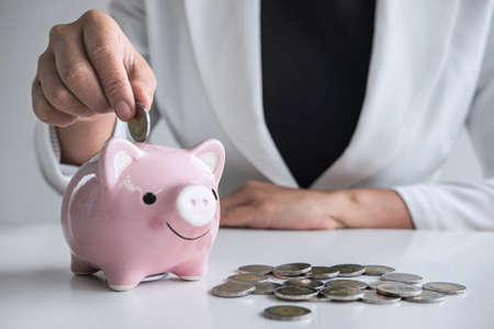 Business woman putting coin into pink piggy bank for planning step up growing business to profit and saving with piggy bank, Saving money for future plan and retirement fund concept.の写真素材