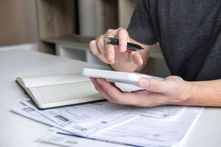 Images of stacking coin pile and Husband using calculator to calculating expenditure receipt bills of various activity cost and expenses in home office and written make report to plan of spent.の写真素材