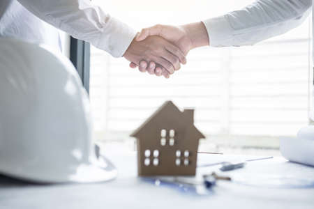 Handshake of collaboration, Construction engineering or architect discuss a blueprint and building model while checking information on sketching, meeting for architectural project of partner.の写真素材
