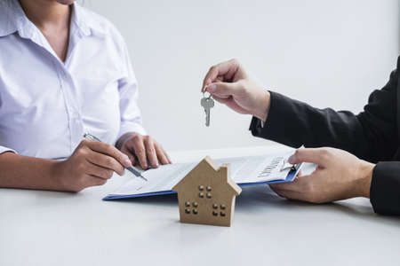 Estate agent giving house keys to client after signing agreement contract real estate with approved mortgage application form, concerning mortgage loan offer for and house insurance.の写真素材