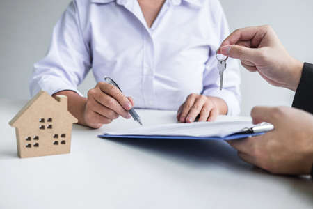 Estate agent giving house keys to client after signing agreement contract real estate with approved mortgage application form, concerning mortgage loan offer for and house insurance.の写真素材