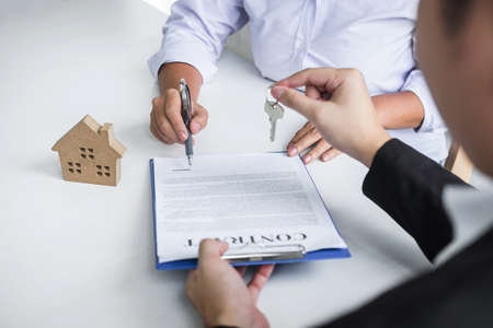 Estate agent giving house keys to client after signing agreement contract real estate with approved mortgage application form, concerning mortgage loan offer for and house insurance.の写真素材
