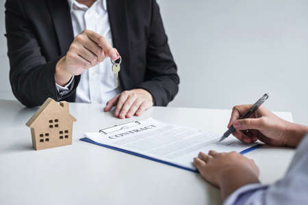 Estate agent giving house keys to client after signing agreement contract real estate with approved mortgage application form, concerning mortgage loan offer for and house insurance.の写真素材
