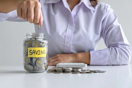 Woman putting coin in bottle for step up growing business to profit and saving with money box, Saving money for future plan and retirement fund concept.の写真素材