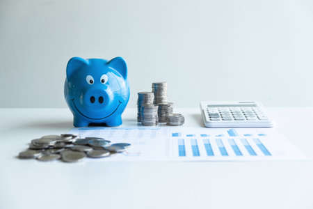 Images of stacking coins pile and blue smiling piggy bank to growing and savings with money box, Saving money for future plan and retirement fund concept.の写真素材