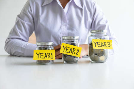 Woman putting coin in piggy bank for step up growing business to profit of each years and saving with piggy bank, Saving money for future plan and retirement fund concept.の写真素材