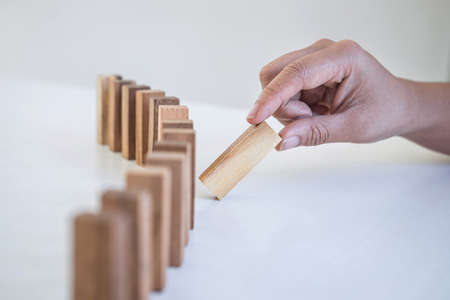 Risk and Strategy in Business, Image of hand gambling placing wooden block on a line of domino,...