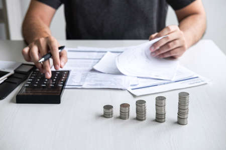 Images of stacking coin pile and Husband using calculator to calculating expenditure receipt bills of various activity cost and expenses in home office and written make report to plan of spent.の写真素材