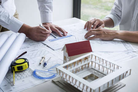Construction engineering or architect discussing a blueprint and building model while checking...