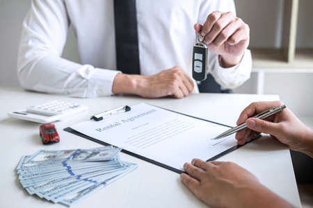 Car rent agent manager sending key of new car giving to woman client after signing good deal agreement contract, renting considering vehicle.の写真素材