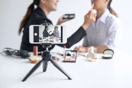 Business online on social media, Two Beautiful Woman Blogger is showing present tutorial beauty cosmetic product and broadcast live streaming video to social network while recording teaching online.の写真素材
