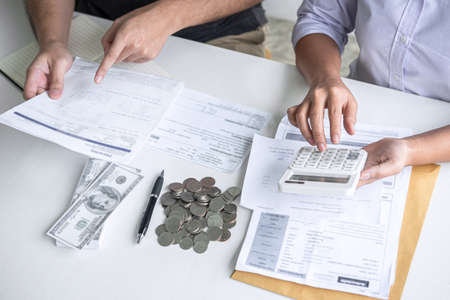 Images of Husband and wife using calculator to calculating expenditure receipt bills of various activity cost and expenses in home office and written make report to plan of spent in future.の写真素材