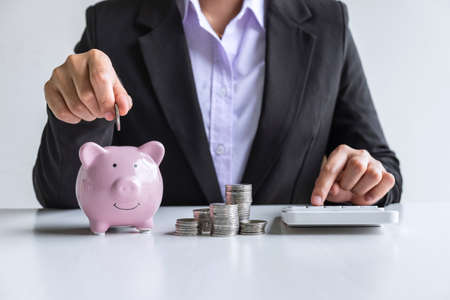 Woman putting coin in pink piggy bank for step up growing business to profit and saving with piggy bank, Saving money for future plan and retirement fund concept.の写真素材