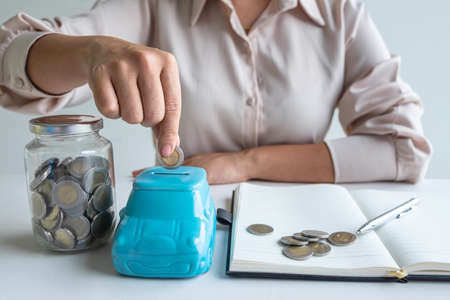 Woman putting coin in blue piggy bank for step up growing business to profit and saving with piggy bank, Saving money for future plan and retirement fund concept.の写真素材
