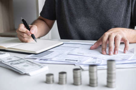 Images of stacking coin pile and Husband using calculator to calculating expenditure receipt bills of various activity cost and expenses in home office and written make report to plan of spent.の写真素材