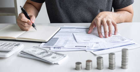 Images of stacking coin pile and Husband using calculator to calculating expenditure receipt bills of various activity cost and expenses in home office and written make report to plan of spent.の写真素材