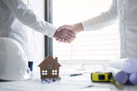 Handshake of collaboration, Construction engineering or architect discuss a blueprint and building model while checking information on sketching, meeting for architectural project of partner.の写真素材