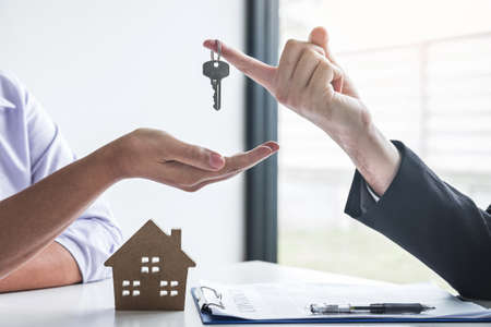 Estate agent giving house keys to client after signing agreement contract real estate with approved mortgage application form, concerning mortgage loan offer for and house insurance.の写真素材