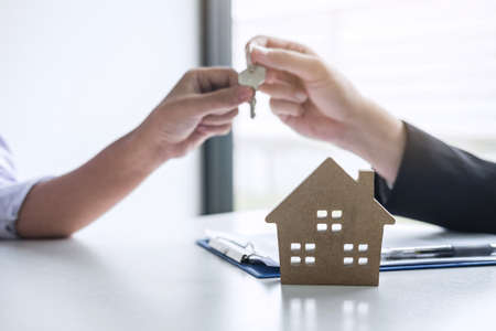 Estate agent giving house keys to client after signing agreement contract real estate with approved mortgage application form, concerning mortgage loan offer for and house insurance.の写真素材