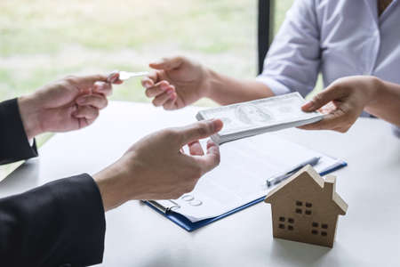 Estate agent giving house keys to client after signing agreement contract real estate with approved mortgage application form, concerning mortgage loan offer for and house insurance.の写真素材