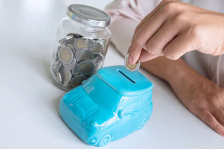 Woman putting coin in blue piggy bank for step up growing business to profit and saving with piggy bank, Saving money for future plan and retirement fund concept.の写真素材