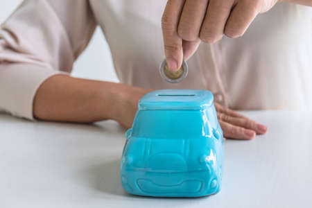 Woman putting coin in blue piggy bank for step up growing business to profit and saving with piggy bank, Saving money for future plan and retirement fund concept.の写真素材