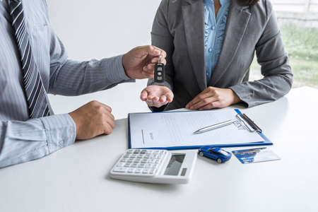 Car rent agent manager holding key of new car giving to woman client after signing good deal agreement contract, renting considering vehicle.の写真素材