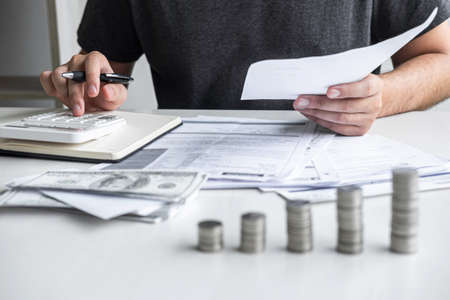 Images of stacking coin pile and Husband using calculator to calculating expenditure receipt bills of various activity cost and expenses in home office and written make report to plan of spent.の写真素材
