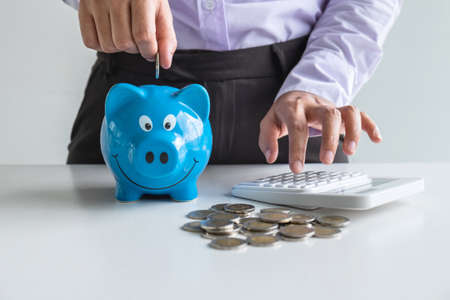 Woman putting coin in blue piggy bankの写真素材