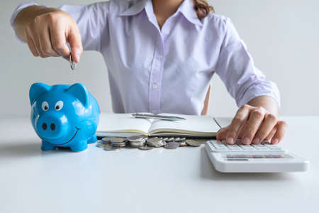 Woman putting coin in blue piggy bankの写真素材