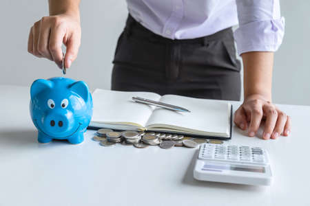 Woman putting coin in blue piggy bankの写真素材