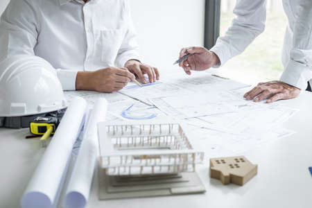 Construction engineering or architect discussing a blueprint and building model while checking information on sketching meeting for architectural project in work site.の写真素材