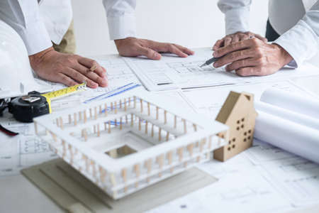 Construction engineering or architect discussing a blueprint and building model while checking information on sketching meeting for architectural project in work site.の写真素材