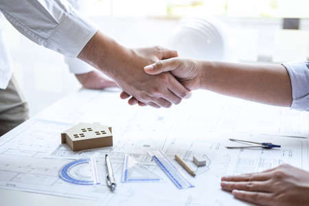 Handshake of collaboration, Construction engineering or architect discuss a blueprint and building model while checking information on sketching, meeting for architectural project of partner.の写真素材