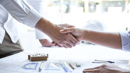 Handshake of collaboration, Construction engineering or architect discuss a blueprint and building model while checking information on sketching, meeting for architectural project of partner.の写真素材
