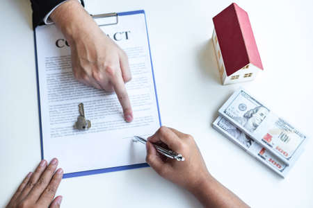 Estate agent broker pointing contract form to client signing agreement contract real estate with approved mortgage application form, buying or concerning mortgage loan offer for and house insurance.の写真素材