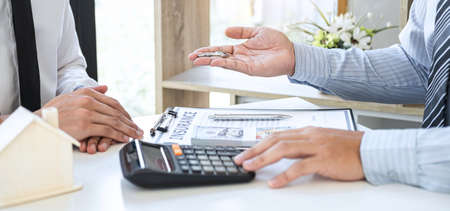 Estate agent giving house keys to client after signing agreement contract real estate with approved mortgage application form, concerning mortgage loan offer for and house insurance.の写真素材