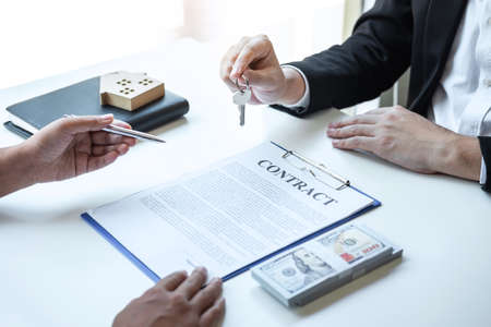 Estate agent giving house keys to client after signing agreement contract real estate with approved mortgage application form, concerning mortgage loan offer for and house insurance.の写真素材