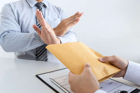 Anti bribery and corruption concept, Business man refusing and don't receive money banknote in envelope offer from business people to accept agreement contract of investment deal.の写真素材